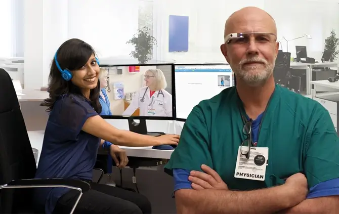 A doctor and a medical scribe in a healthcare setting. The doctor is standing, while the medical scribe, a girl, is sitting in front of her computer. The girl is wearing a blue headset, and the doctor's face is equipped with Google Glass.